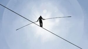 Minimalist photograph of a silhouetted tightrope walker from below.