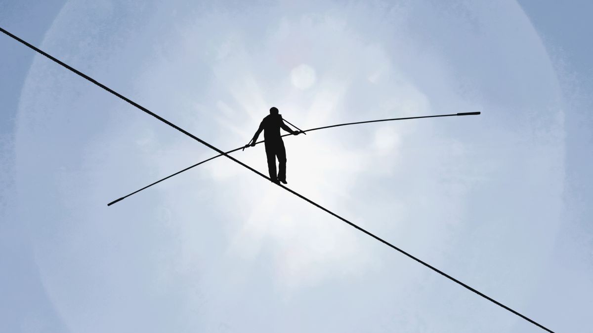 Minimalist photograph of a silhouetted tightrope walker from below.