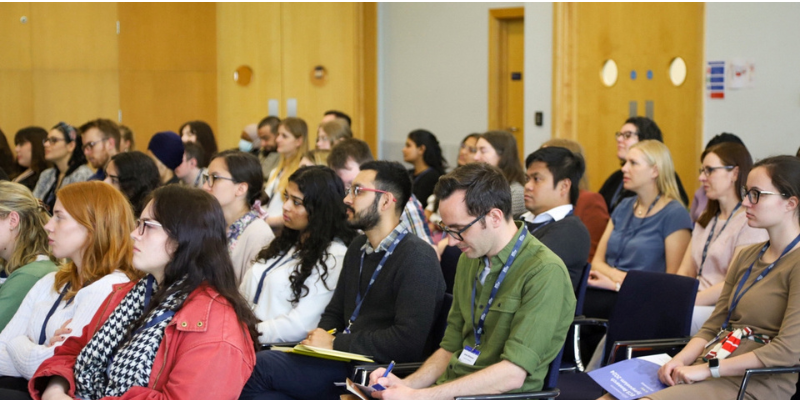 A crowd of people, seated, listening to a talk
