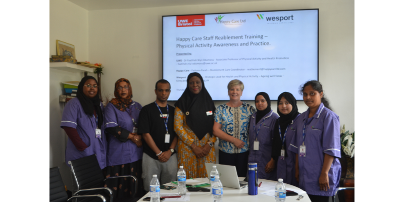 Happy Care staff and trainers from UWE Bristol and Wesport stand together after a reablement training session, with a presentation slide about physical activity awareness shown on the screen behind them.